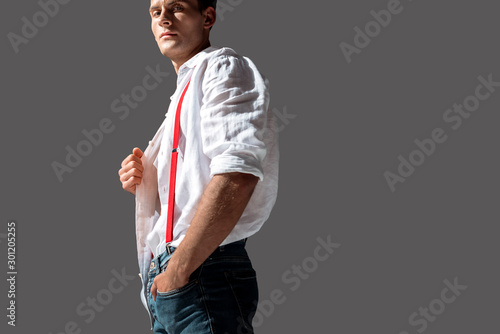 handsome man touching white shirt while standing with hand in pocket isolated on grey