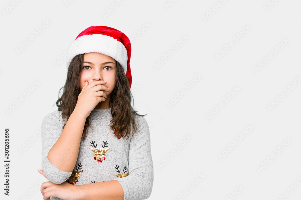Little girl celebrating christmas day thoughtful looking to a copy space covering mouth with hand. Little girl celebrating christmas day thoughtful looking to a copy space covering mouth with hand.