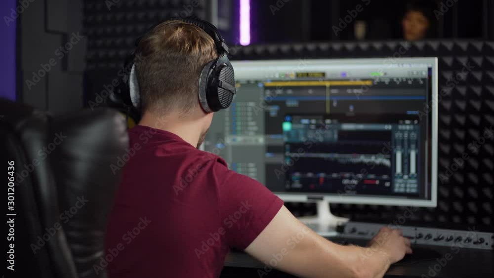 Back view zoom in of male sound producer in earphones using professional software on computer to record song in music production studio Back view zoom in of male sound producer in earphones using professional software on computer to record song in music production studio