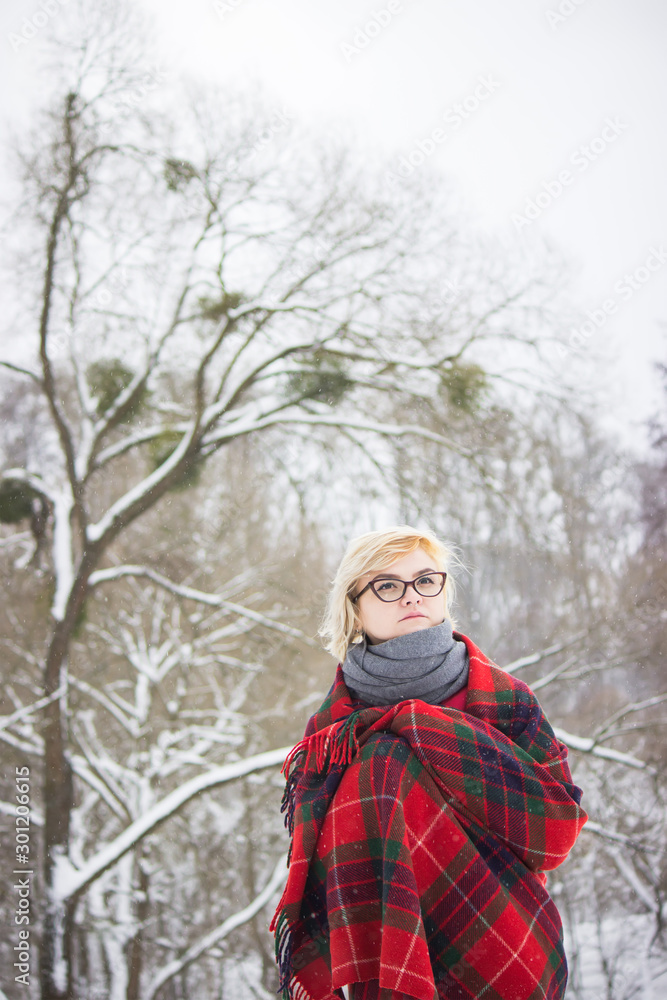 girl in glasses and red plaid stands at winter trees