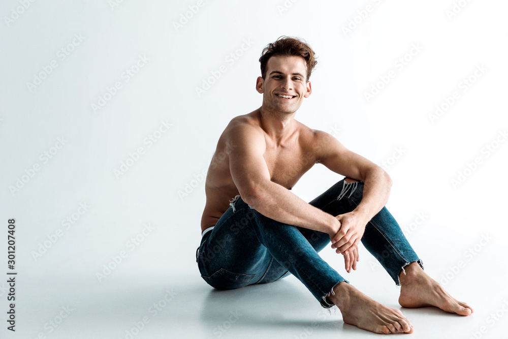 happy shirtless man with barefoot sitting on white