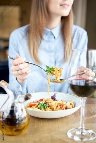 Woman eats Italian pasta with seafood and tomato sauce. Pasta Gamberini. Close-up tagliatelle wind it around a fork with a spoon. Parmesan cheese