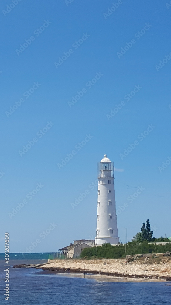 Lighthouse near the shore on a Sunny day. Calm sea, the lighthouse and blue sky.