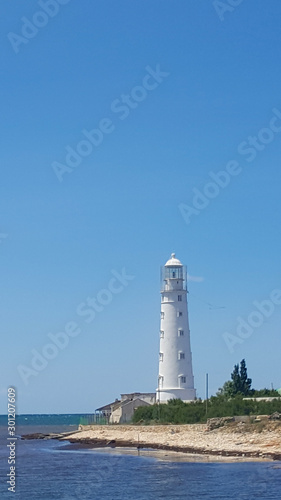 Lighthouse near the shore on a Sunny day. Calm sea, the lighthouse and blue sky.