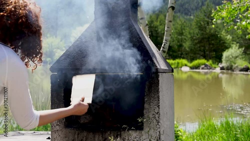 Girl blows coals and fans embers in the barbecue bbq brazier. Outdoors picnic concept. photo