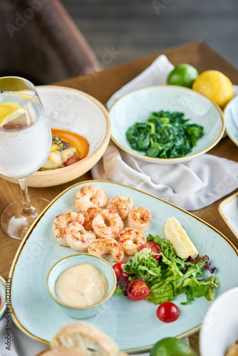 Dish shrimp with arugula and lemon. BBQ seafood. Restaurant menu. Variety of dishes on the table. Restaurant menu.