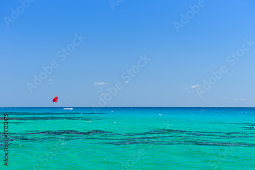 Water of the tropical turquoise sea with a boat and a red parachute. Parasailing.