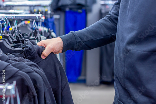 A man choosing sweatshirt or hoodie at the modern sport store. Shopping and season sale concept.