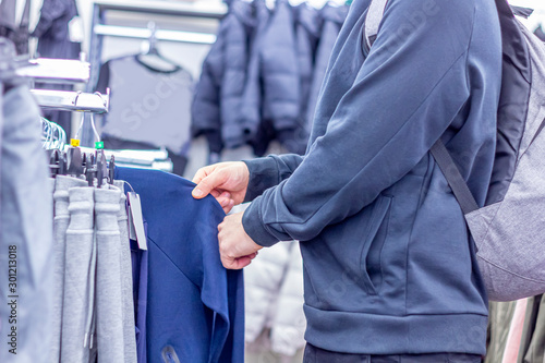 A man choosing sweatshirt or hoodie at the modern sport store. Shopping and season sale concept.