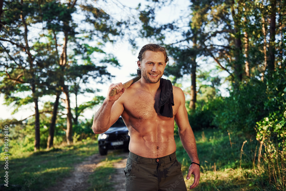 Close up portrait of woodsman with axe in hand. Handsome shirtless man with muscular body type is in the forest at daytime Close up portrait of woodsman with axe in hand. Handsome shirtless man with muscular body type is in the forest at daytime