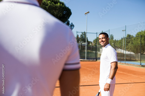 Man in sportswear smiling and looking at crop competitor while standing on tennis court photo