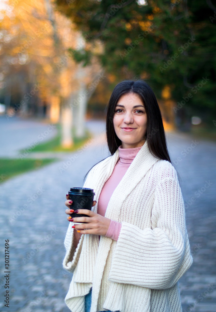 young female in white cardigan in the autumn park with black cup of coffee young female in white cardigan in the autumn park with black cup of coffee