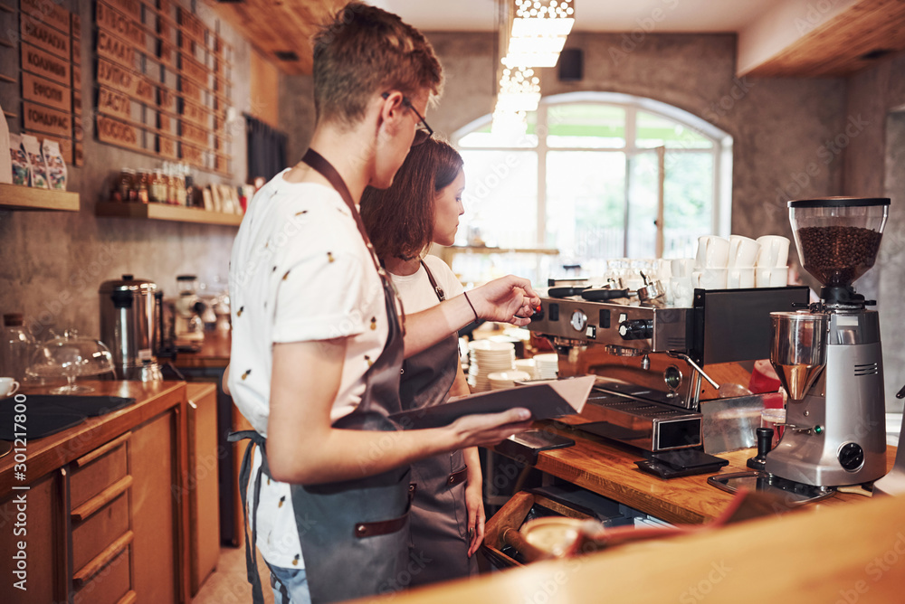 With notepad. Talking with each other. Two young cafe workers indoors. Conception of business and service With notepad. Talking with each other. Two young cafe workers indoors. Conception of business and service