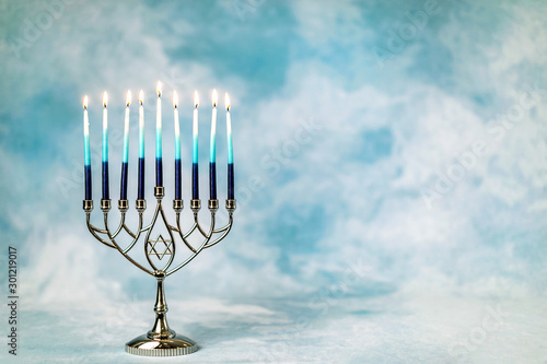 A silver menorah for the Jewish holiday Hanukkah with burning glowing eight candles on fire lit up on a blue background with copy space photo