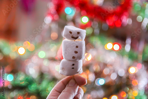 Funny marshmallow snowman on decorated Christmas tree blurred background. photo