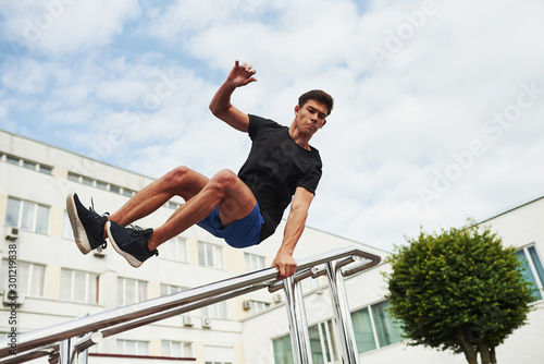 Silver colored railings. Young sports man doing parkour in the city at sunny daytime