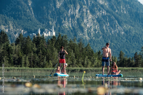 Family paddle boarding on lake Bannwaldsee, Castle Neuschwanstein in the, Fuessen, Germany photo