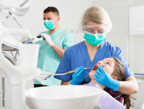 Female dentist performing treatment for girl with assistant
