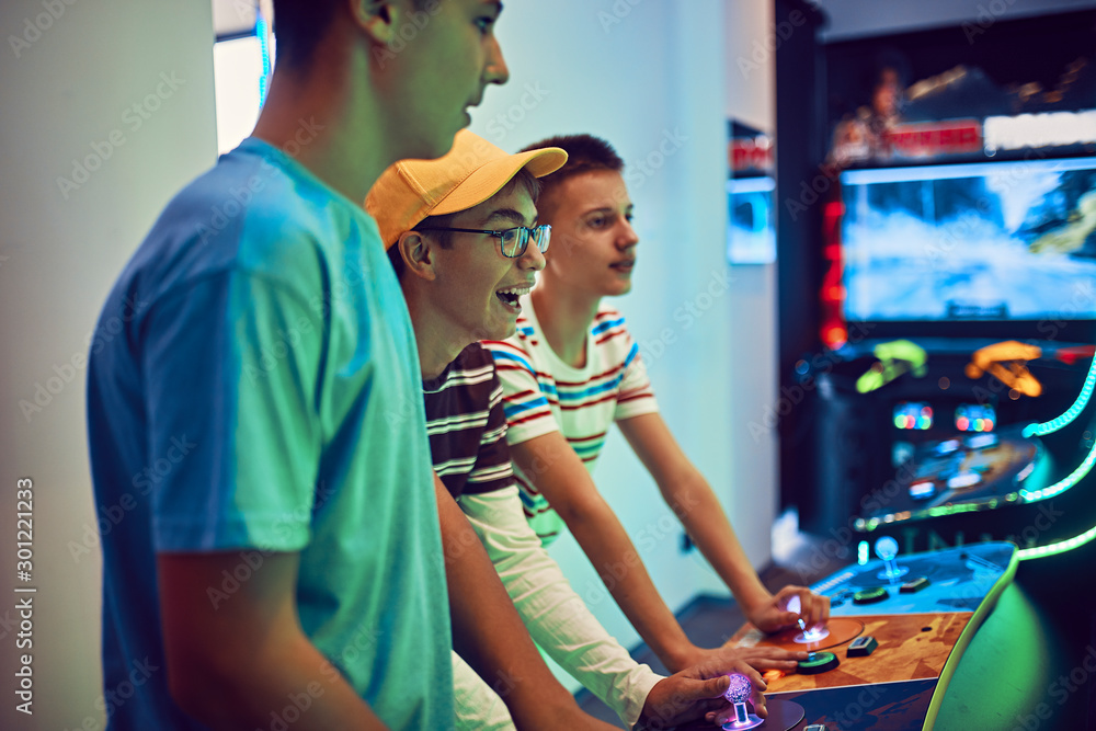 Teenage friends playing with a gaming machine in an amusement arcade Teenage friends playing with a gaming machine in an amusement arcade