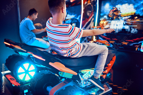 Teenage friends playing with a driving simulator in an amusement arcade photo