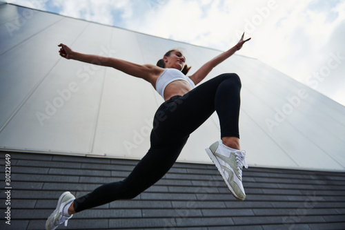 Bottom view. Young sportswoman doing parkour in the city at sunny daytime