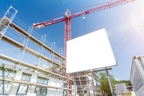Blank white billboard in front of construction site with scaffolding and crane