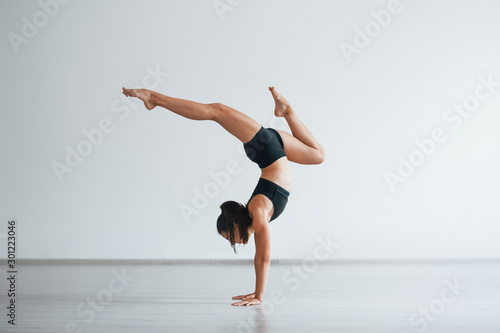 Doing hand stand. Young sporty woman in black clothes with slim body type in the healthy center doing exercises