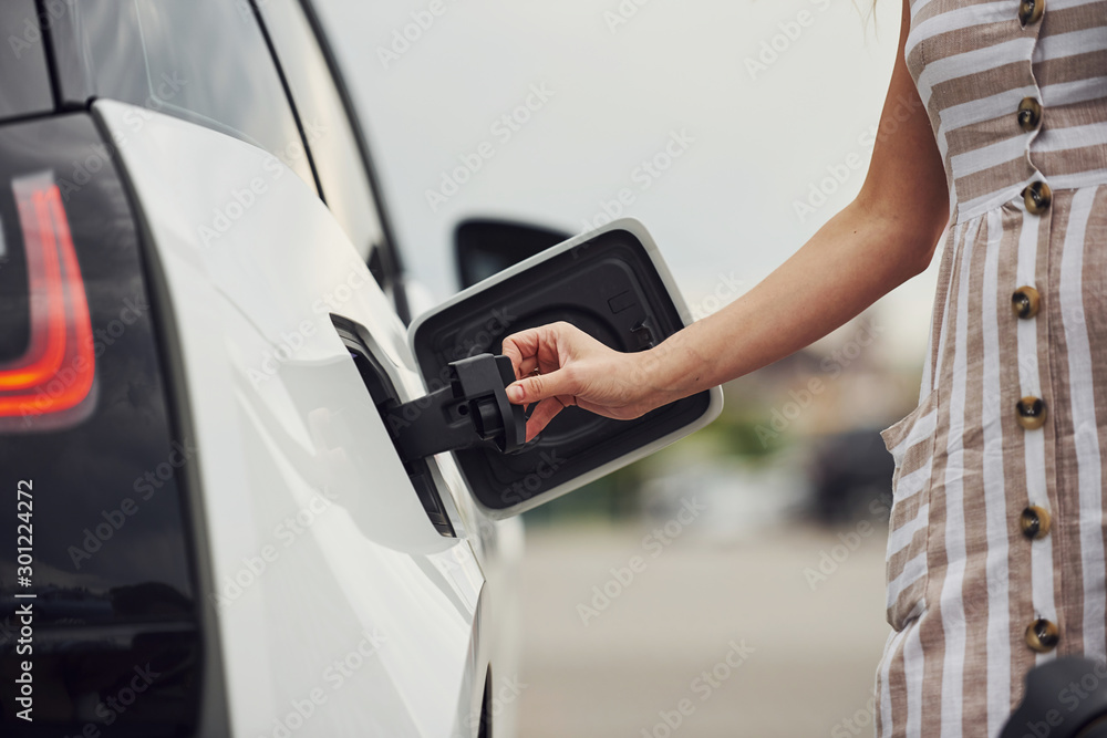 Woman on the electric cars charge station at daytime. Brand new vehicle Woman on the electric cars charge station at daytime. Brand new vehicle