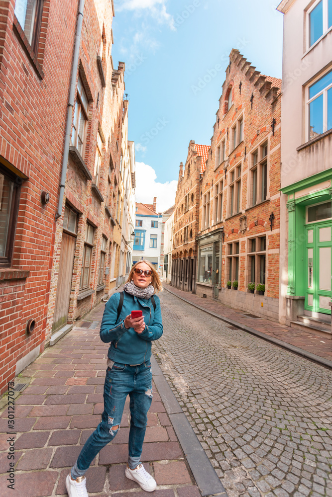 Woman tourist lost in the streets of the city and is looking on his phone how to get further, Bruges, Belgium