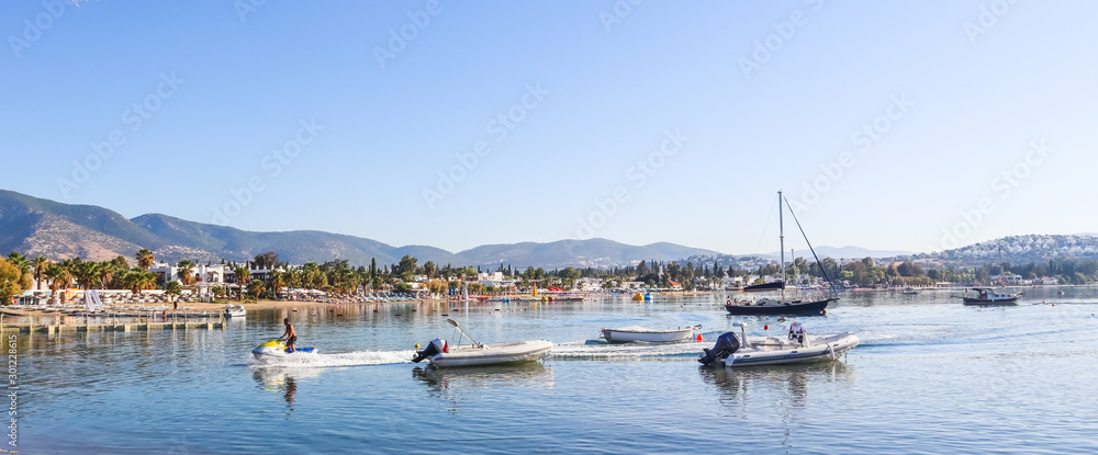 Fototapeta premium Beautiful bay with calm water, sandy beach, boats and yachts. Small town and green mountains on the coast of the Aegean sea