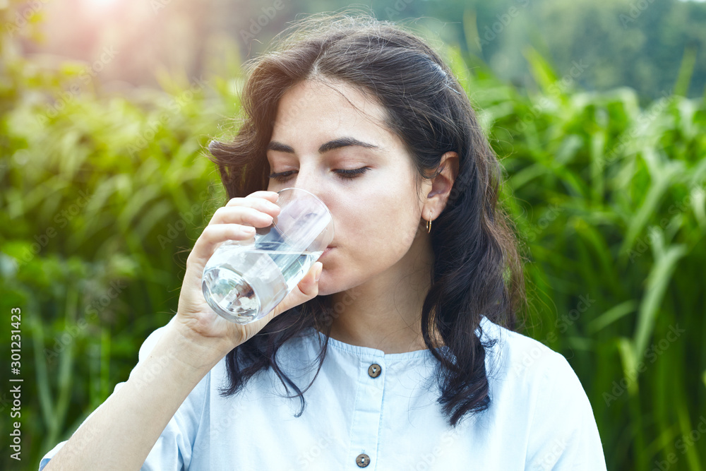 healthy beautiful young brunette woman holding glass of clear pure water and drinking outside, morning light healthy beautiful young brunette woman holding glass of clear pure water and drinking outside, morning light
