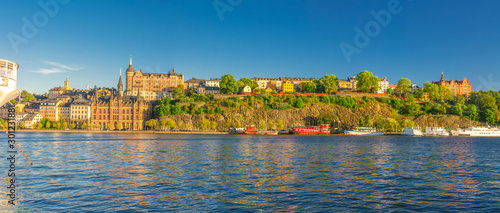 Panoramic view of Sodermalm island with Multicolor colorful fishing boats and ships on Lake Malaren, typical traditional buildings, Monteliusvagen view platform, clear blue sky, Stockholm, Sweden
