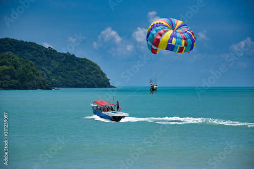 Parasailing on the waves of the azure Andaman sea under the blue sky near the shores of the sandy beautiful exotic and stunning Cenang beach in Langkawi island,