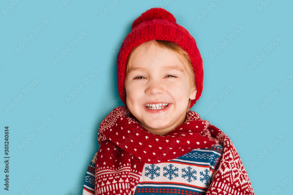 Happy child in red hat and a scarf on a blue background . Christmas time. Happy child in red hat and a scarf on a blue background . Christmas time.