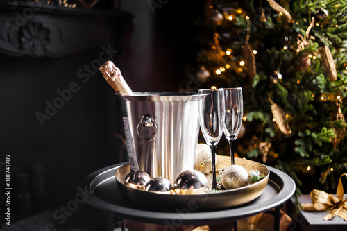 Champagne bottle in freezer bucket with glasses on dark background.