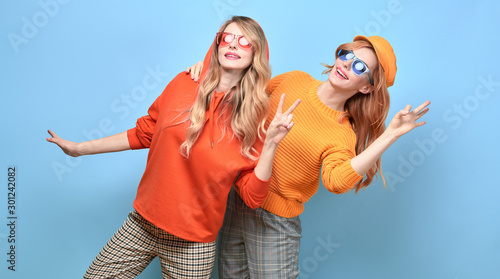 Fashionable woman in stylish outfit, makeup having fun dance. Two happy blonde redhead tomboy girl, trendy orange jumper, hoody, fashion hair. Cheerful sister friend, funny colorful concept © evgenij918