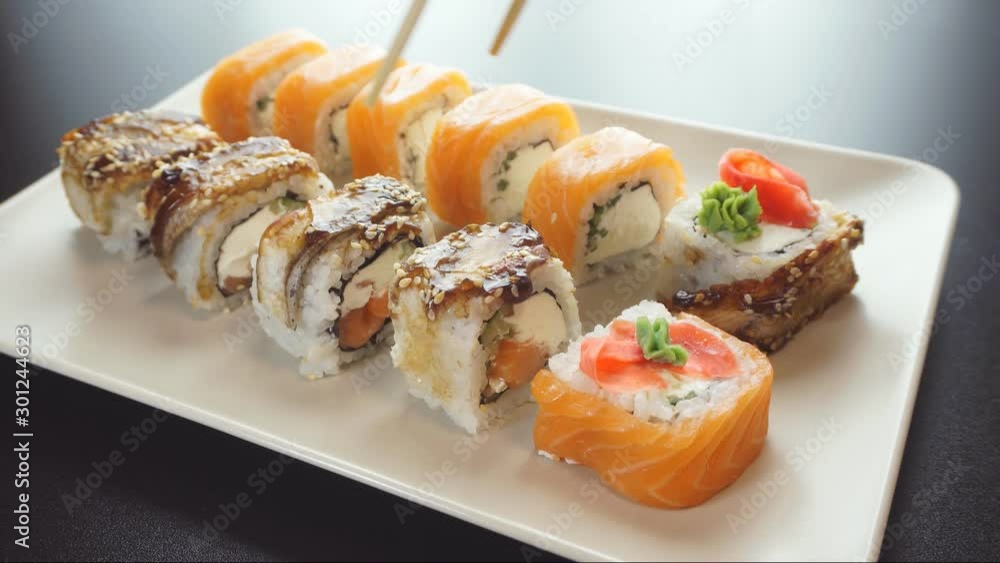Female hands holding chopsticks with roll. Sushi rolls on a plate. Female hands holding chopsticks with roll. Sushi rolls on a plate.