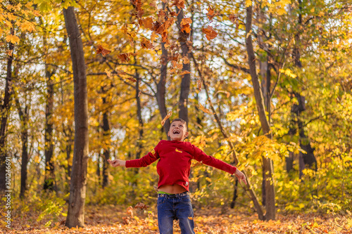 young guy in red laughs in the autumn forest and bounced up throws yellow leaves © Chernobrovin