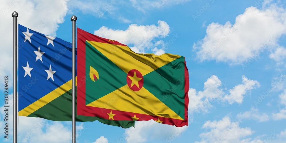 Solomon Islands and Grenada flag waving in the wind against white cloudy blue sky together. Diplomacy concept, international relations. Solomon Islands and Grenada flag waving in the wind against white cloudy blue sky together. Diplomacy concept, international relations.