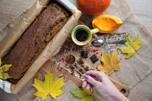 Chocolate cake in a pan made from pumpkin with black coffee and woman's hand. Vintage composition on the wooden table and autumn arrangement. 
