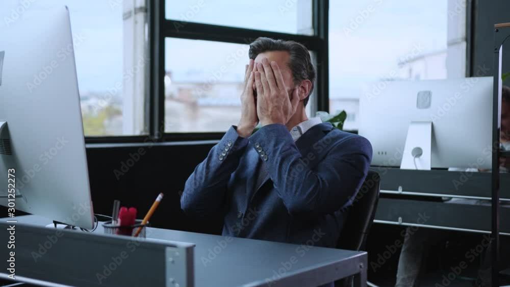 Overwhelmed business manager in despair putting off his glasses feeling tired of excessive workload relaxing in chair at office workspace.