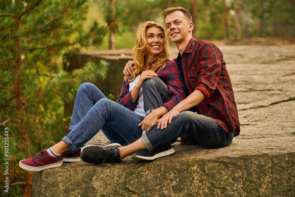 Couple of tourists exploring a new places. Handsome couple on nature sits on canyon rock at forest background. Couple of tourists exploring a new places. Handsome couple on nature sits on canyon rock at forest background.