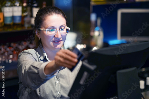 Professional bartender woman in eyeglases registrating new order by cash register. Restaurant worker registrating new order by cash-register. The concept of service.  photo