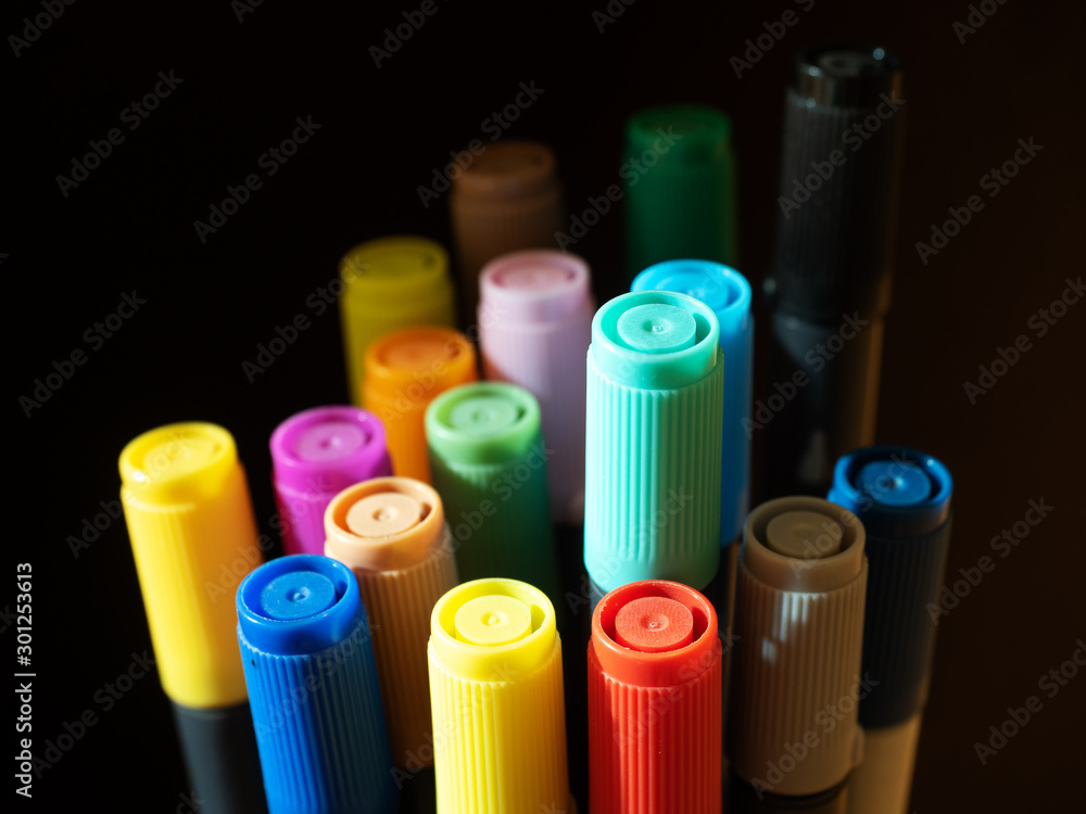 Large group of colored felt-tip pens with caps on a dark background