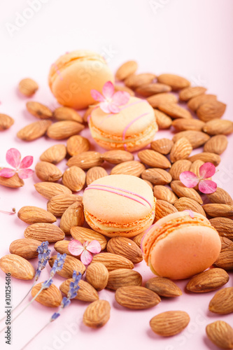 Orange macarons or macaroons cakes with almond nuts on pastel pink background. side view, close up.