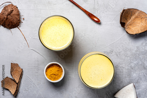 Golden milk. Coconut milk with turmeric, spices and honey in glasses, coconut and turmeric powder on a gray background, top view, flat lay. Indian drink haldi ka doodh, vegan food. photo