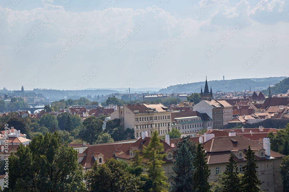 A view of the city's landscaping with many roofs and green trees with a distant horizon in Prague, Czech Republic.