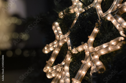 one blurred, selective focused white neon led snowflake on a Christmas tree, festive greeting background with copy space for text and design
