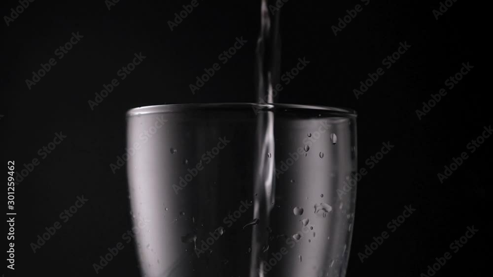 Ordinary tap water is poured into a transparent glass with drops on a black background. Ordinary tap water is poured into a transparent glass with drops on a black background.
