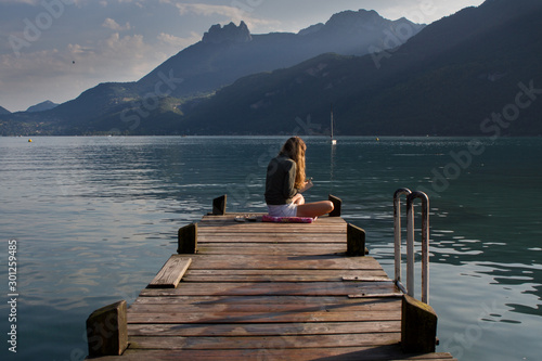 Lonely girl sitting at the pier of lake annecy with mobile phone in her hand